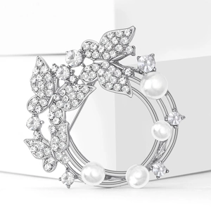 Élégante broche couronne papillon en strass et perles finition argent sur fond blanc