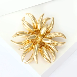 Detailed view of a golden fireworks alloy brooch with a radiant layered structure on white base