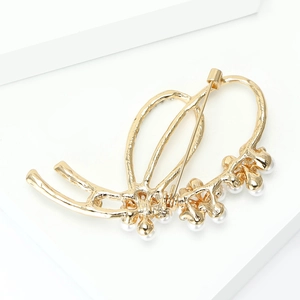 Détail d'une élégante broche dorée avec perles et design d'aile en métal texturé