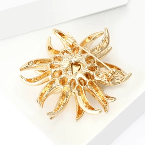 Macro view showing the secure safety pin clasp and hollow back of the gold flower brooch