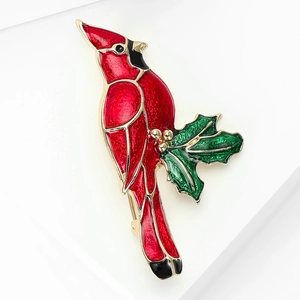 Red cardinal bird enamel brooch with green leaves and gold accents on white platform