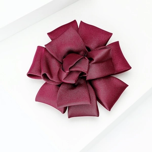 Detail of burgundy satin fabric flower brooch with handmade layered ribbon texture