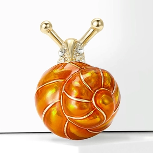 Détail macro d'une broche escargot en émail doré avec finition orange et strass brillants