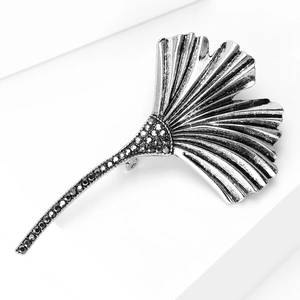 Macro detail of silver ginkgo leaf brooch with black rhinestones on white stairs