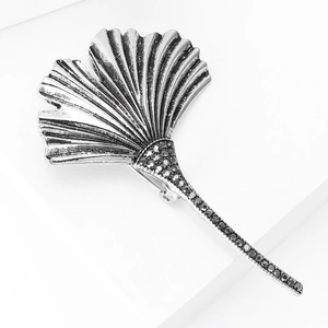 Detailed close-up of a silver ginkgo leaf brooch with black rhinestones on a white stand