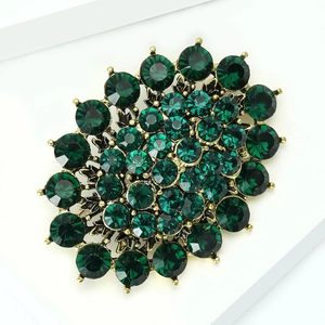 Macro view of vintage gold metal brooch featuring emerald green faceted crystal settings