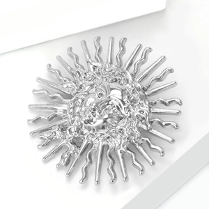 Détail de la broche soleil argentée avec relief de visage sur fond géométrique blanc