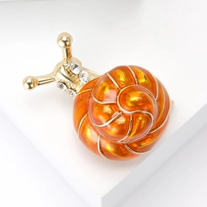 Détail d'une broche escargot dorée avec émail orange et cristaux brillants sur fond blanc