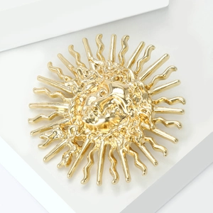 Détail de la broche soleil dorée avec relief de visage sur plateau blanc pour femme