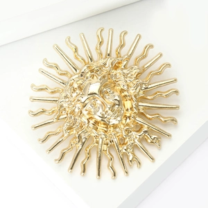 Détail macro d'une broche soleil vintage dorée avec des rayons gaufrés complexes