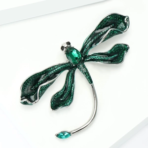 Detailed close-up of a silver dragonfly brooch with green rhinestones and oil dripping