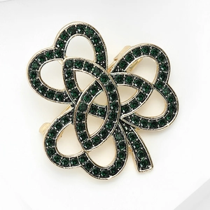 Détail macro d'une broche trèfle dorée ornée de strass pavé verts et design ajouré