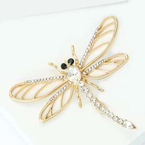 Détail macro de broche libellule dorée avec ailes en émail blanc et strass étincelants