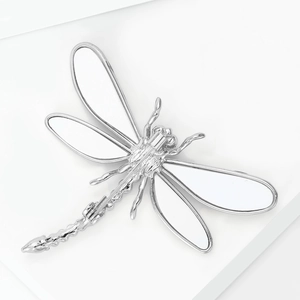 Détail macro d'une élégante broche libellule argentée avec ailes blanches et métal poli