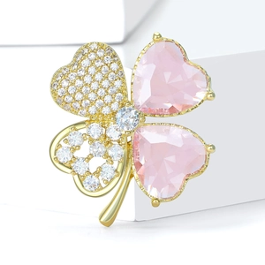 Vue macro d'une broche trèfle dorée avec pierres roses en cœur et détails en zircon blanc