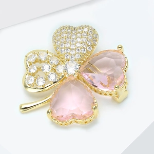 Détail macro d'une broche trèfle dorée avec pierres cœur roses et pavage de zircons