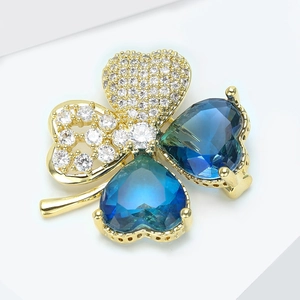 Vue détaillée d'une broche trèfle avec gemmes cœur bleues et base en métal doré