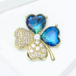 Détail macro d'une broche trèfle dorée avec cristaux bleu foncé et zircons blancs