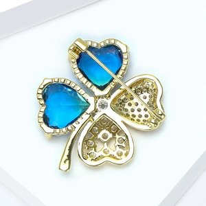 Détail macro d'une broche trèfle dorée avec pierres de cœur bleues et strass