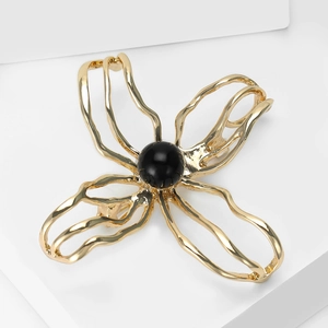 Macro shot of abstract gold flower brooch with black stone on white geometric pedestal