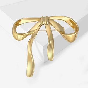 Detail of a large gold bow brooch showing smooth matte texture and back pin fastening