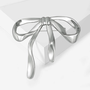 Polished silver alloy bowknot brooch on white geometric stand showing reflective metallic texture
