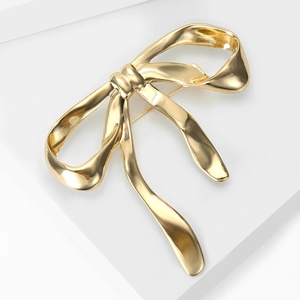 Elegant gold bow brooch with organic polished lines displayed on a white stand