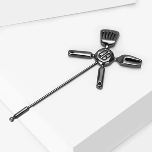 Close-up of industrial style kitchenware brooch with crossed utensils and engraved QB disc