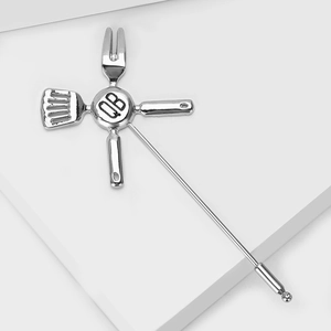 Detailed close-up of a silver kitchen utensil brooch with central QB engraving