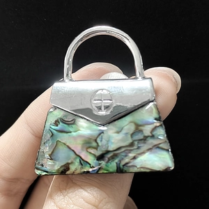 Macro detail of handbag-shaped brooch with iridescent abalone shell inlay and silver finish