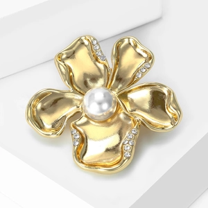 Close-up of golden flower brooch with matte texture, white pearl and crystal accents