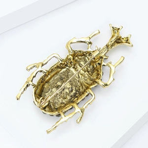 Detailed back view of a gold beetle brooch with metal pin and safety clasp on a white stand