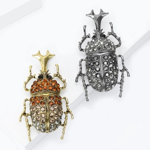 Retro rhinestone beetle brooches in gold and black metal on white stone blocks