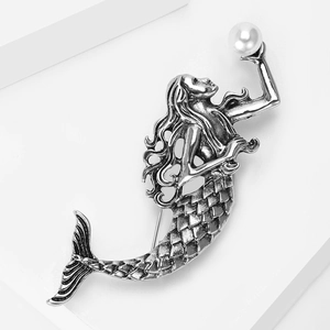 Detailed close-up of retro mermaid brooch with silver texture and white pearl accents
