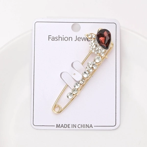 Détail d'une broche épingle dorée avec cristal rouge goutte et strass blancs brillants
