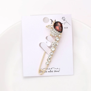 Détail d'une broche dorée avec une grande pierre marron en goutte et strass blancs brillants