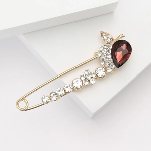 Détail d'une broche dorée ornée d'un grand cristal goutte rouge et de strass étincelants