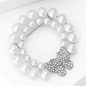 Détail d'une broche couronne argentée avec perles blanches et un papillon en strass brillant