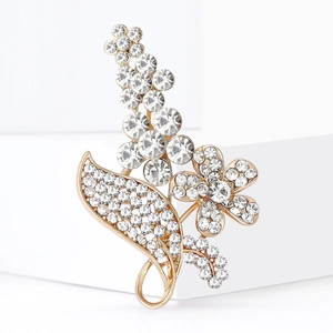 Elegante goldene Blumenbrosche mit Kristallen und Blattdesign auf weißem Podest
