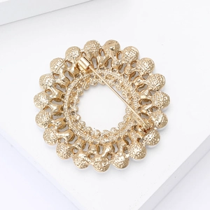 Détail d'une broche couronne dorée montrant la texture ajourée et le fermoir à épingle
