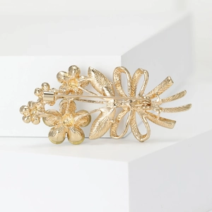 Exquisite gold floral brooch with leaf details and safety pin back on a white stand