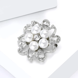 Gros plan d'une broche florale argentée avec perles blanches et cristal central brillant