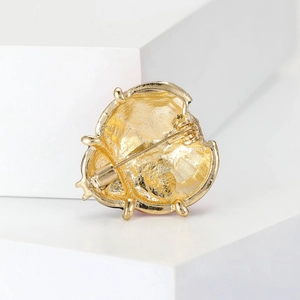Vue arrière d'une broche coccinelle dorée avec épingle de sûreté sur un support blanc