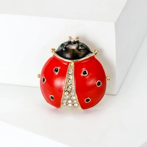 Broche coccinelle en émail rouge avec strass blancs sur support blanc épuré
