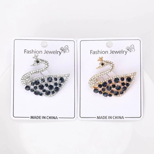 Dettaglio delle spille a cigno con pavé di cristalli e strass blu presentate su carta