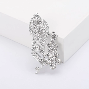 Elegant silver flower leaf brooch with rhinestones displayed on a white platform