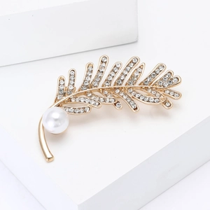 Élégante broche plume dorée avec strass blancs et perle sur un socle blanc épuré