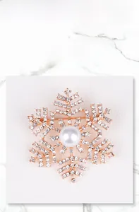 Detailopname van een gouden sneeuwvlok broche met strassteentjes en een centrale parel