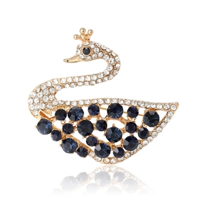 Elegante spilla a cigno dorata con ali in cristallo blu e strass bianchi su sfondo bianco