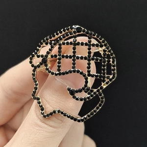 Detailed view of hollow profile head brooch in gold metal with black rhinestones
